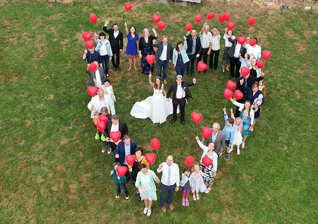 drohnen_eventfotos_04 ein hochzeitspaar steht mit den gaesten in herzform und wird von einer drohne fotografiert